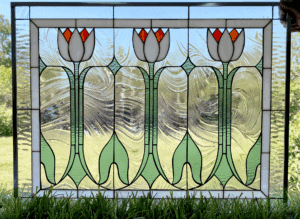 A rectangular stained glass panel featuring three stylized white tulips with orange centers, green stems, and leaves, set against clear textured glass and light green accents with black lead lines.