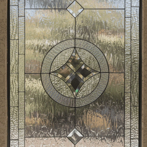A rectangular leaded glass window with a formal, geometric design. It features a central beveled glass cluster of a diamond within a circle, flanked vertically by two smaller diamond bevels, all set against a background of heavily textured clear glass for privacy.