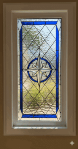 A rectangular clear and blue stained glass panel with a central beveled compass rose design, surrounded by a blue ring. The panel features a background of textured clear diamond-grid glass and solid blue border accents.