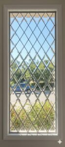 A tall rectangular window with a clear beveled diamond pattern, set in a white frame, offering a view of an outdoor scene.