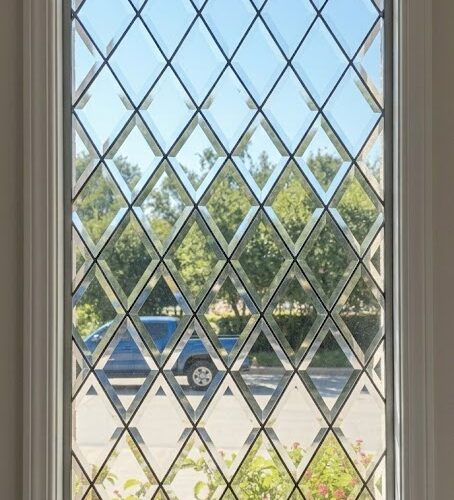 A tall rectangular window with a clear beveled diamond pattern, set in a white frame, offering a view of an outdoor scene.