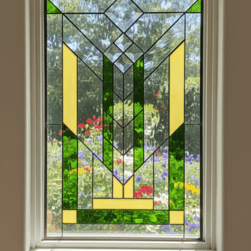 A rectangular Prairie style leaded glass window featuring a symmetrical, geometric design. The pattern consists of strong vertical lines in green and golden-yellow glass, accented by clear beveled chevrons, all set against a clear, textured background.