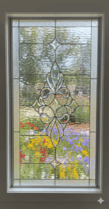 A rectangular leaded glass window featuring a large, intricate, and symmetrical beveled glass cluster as its centerpiece. The ornate cluster is composed of flowing, curved shapes and is set against a background of clear, textured privacy glass with a distinct border.
