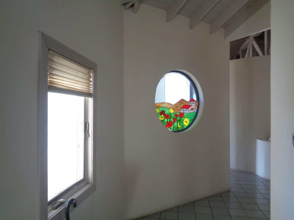 round porthole window fitted with a "wildflower & hills" stained glass insert