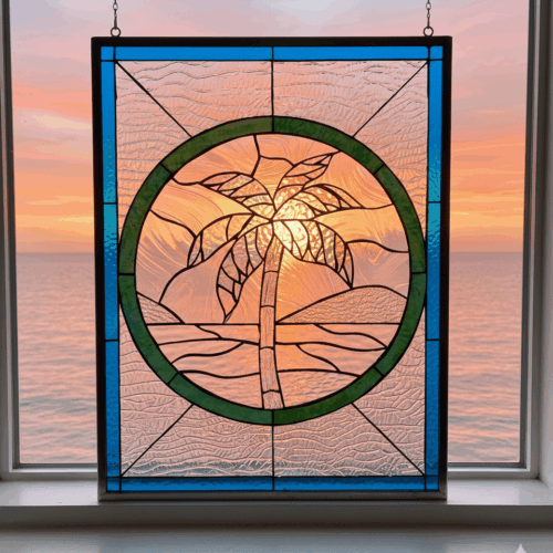 A rectangular stained glass panel depicting a coastal scene. A central green circle frames a stylized palm tree on a beach, crafted from clear, iridescent, and textured glass. The entire piece is bordered with vibrant blue textured glass.