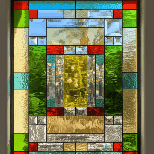 A rectangular Mission style leaded glass window with a symmetrical, geometric design. The architectural pattern is composed of numerous clear beveled glass pieces alongside textured colored glass in shades of green, red, blue, and gold.