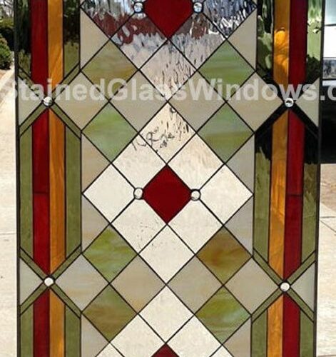 A rectangular, vertically oriented stained glass panel featuring an Art Deco geometric design. The central section has a diamond pattern with white, light green, and clear textured glass, accented by three prominent red diamond shapes and small clear circular glass jewels. The top and bottom borders contain horizontal and vertical bands of red, orange, and green glass, with curved corner elements in cream and green.