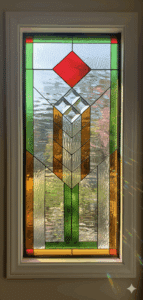 A rectangular Prairie Mission style leaded glass window. The symmetrical, geometric design features a central column of clear bevels and green glass, flanked by amber glass, and topped with a single red diamond accent, all on a clear textured background.