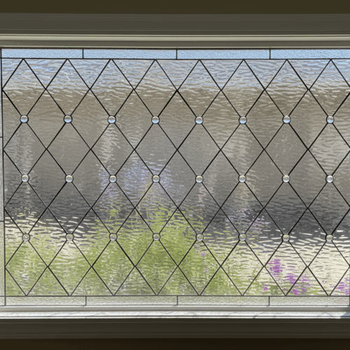 A rectangular leaded glass window with a classic diamond lattice pattern. The design is crafted from clear, textured privacy glass and is accented with small, circular, faceted glass jewels at the intersections of the lead lines.