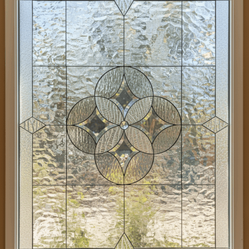 A rectangular leaded glass window with a symmetrical, geometric design. The centerpiece is a floral medallion made of four interlocking circles, featuring a central glass jewel and patterned beveled glass. The design is crafted entirely from clear glass with various textures for privacy.