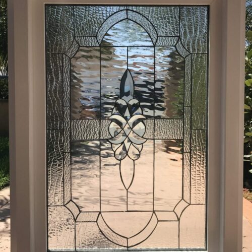 A rectangular white-framed insulated window featuring a leaded clear stained glass panel. It has a central beveled floral-like motif, bordered by intricate patterns of wavy water glass and hammered clear textures.