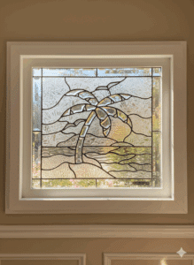 A rectangular leaded stained glass panel depicting a stylized palm tree with clear beveled glass fronds and trunk, set against a background of textured clear glass depicting ocean and sky, framed in white.