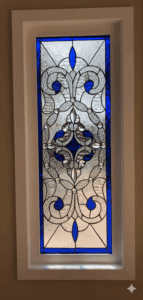 A rectangular stained glass panel featuring a symmetrical, ornate design. It combines clear textured and beveled glass with vibrant cobalt blue accents in scroll and teardrop shapes, all set within a dark leaded framework. The pattern resembles stylized fleur-de-lis and organic forms.