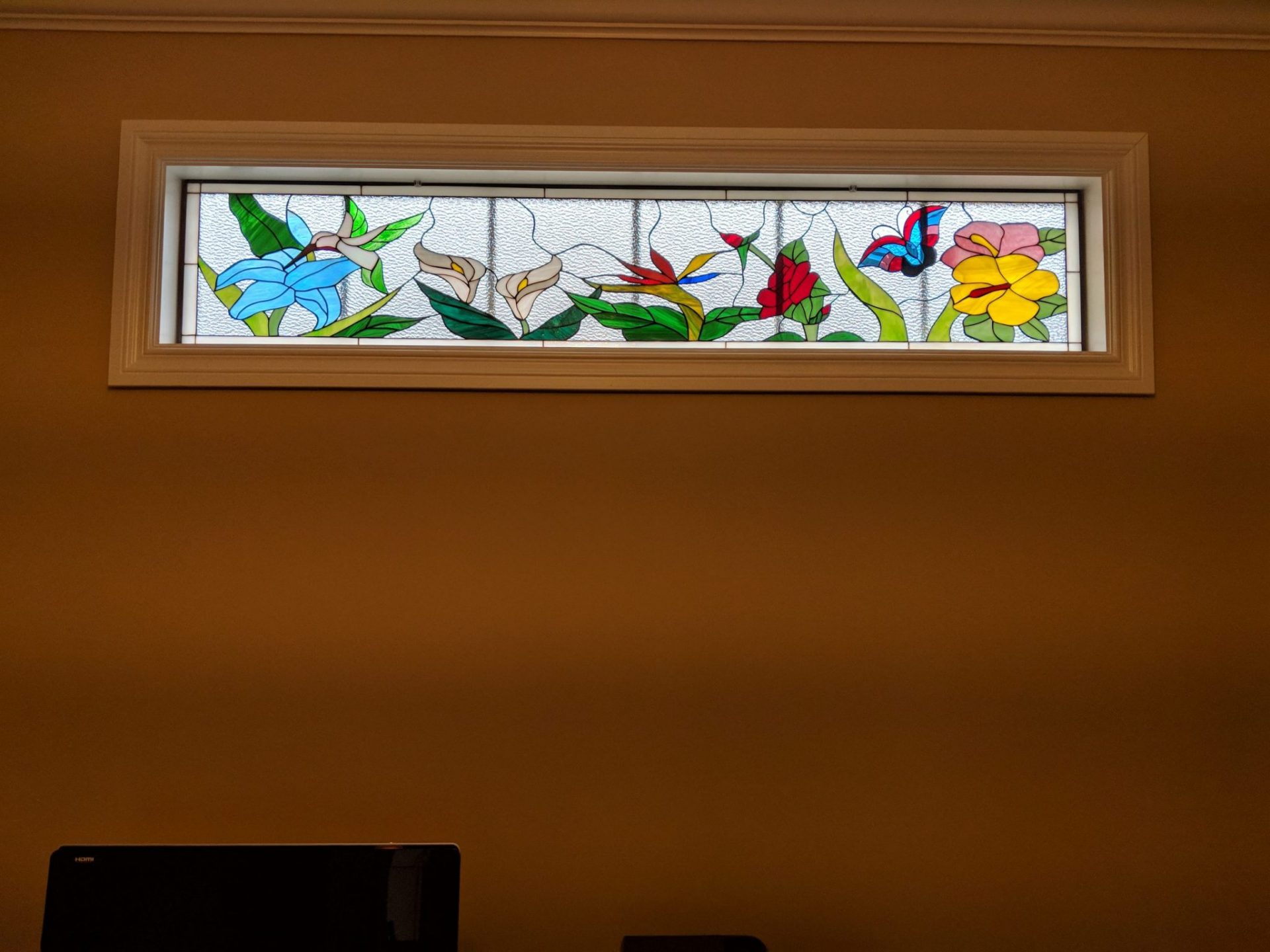 Colorful hummingbird and flower transom window installed in front of the current mullions