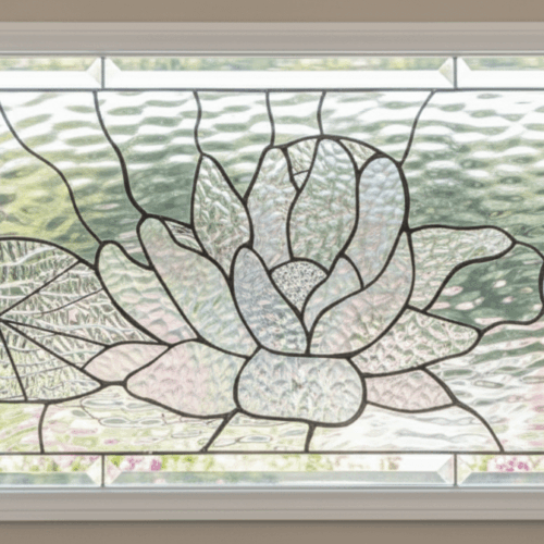 A rectangular stained glass transom window depicting a serene pond scene. The design features a central lotus flower, a lily pad to the left, and a dragonfly to the right. The entire panel is crafted from various types of clear, textured glass with a beveled glass border.