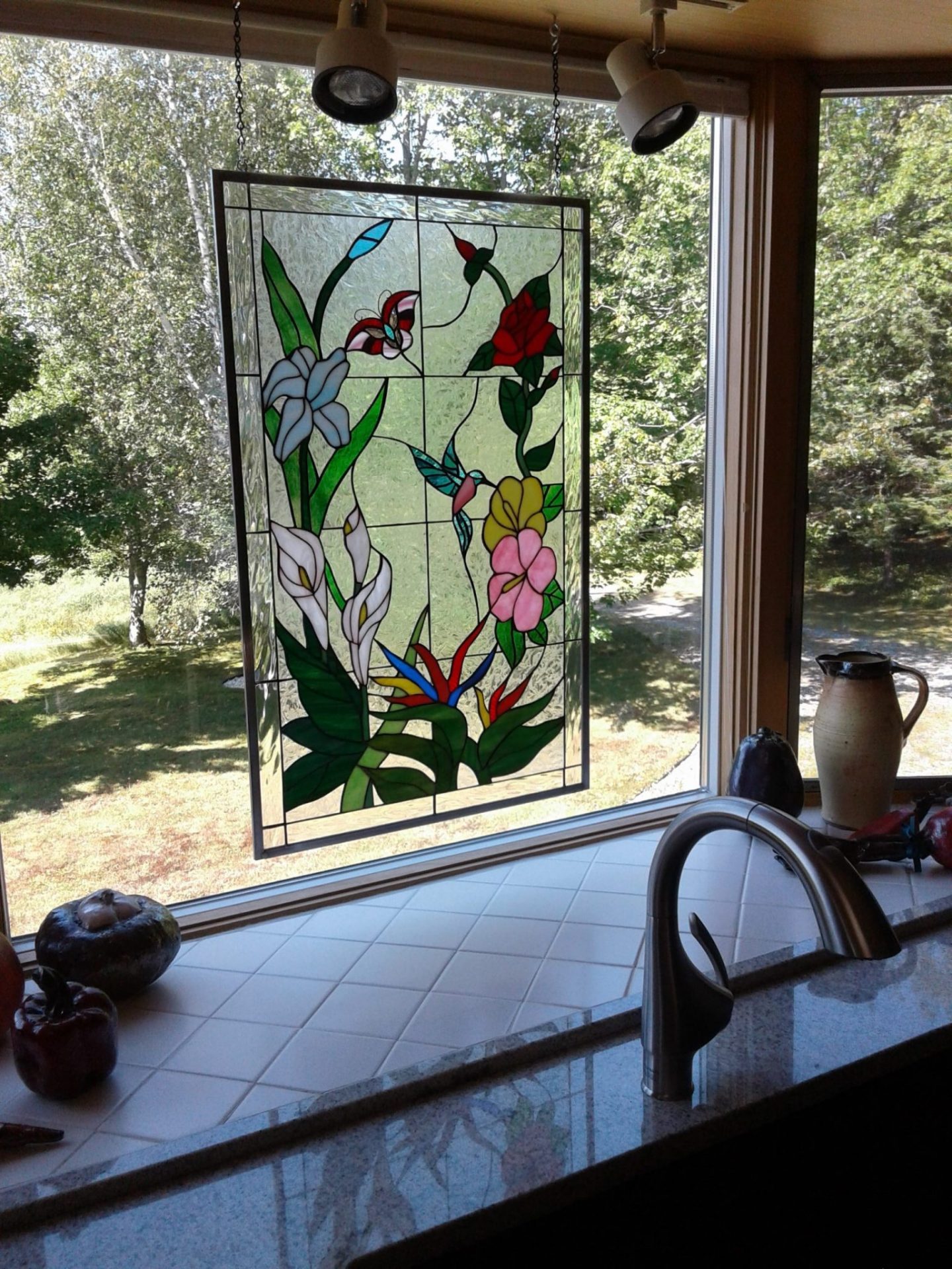 colorful hummingbirds and flowers stained glass panel hung in a kitchen window