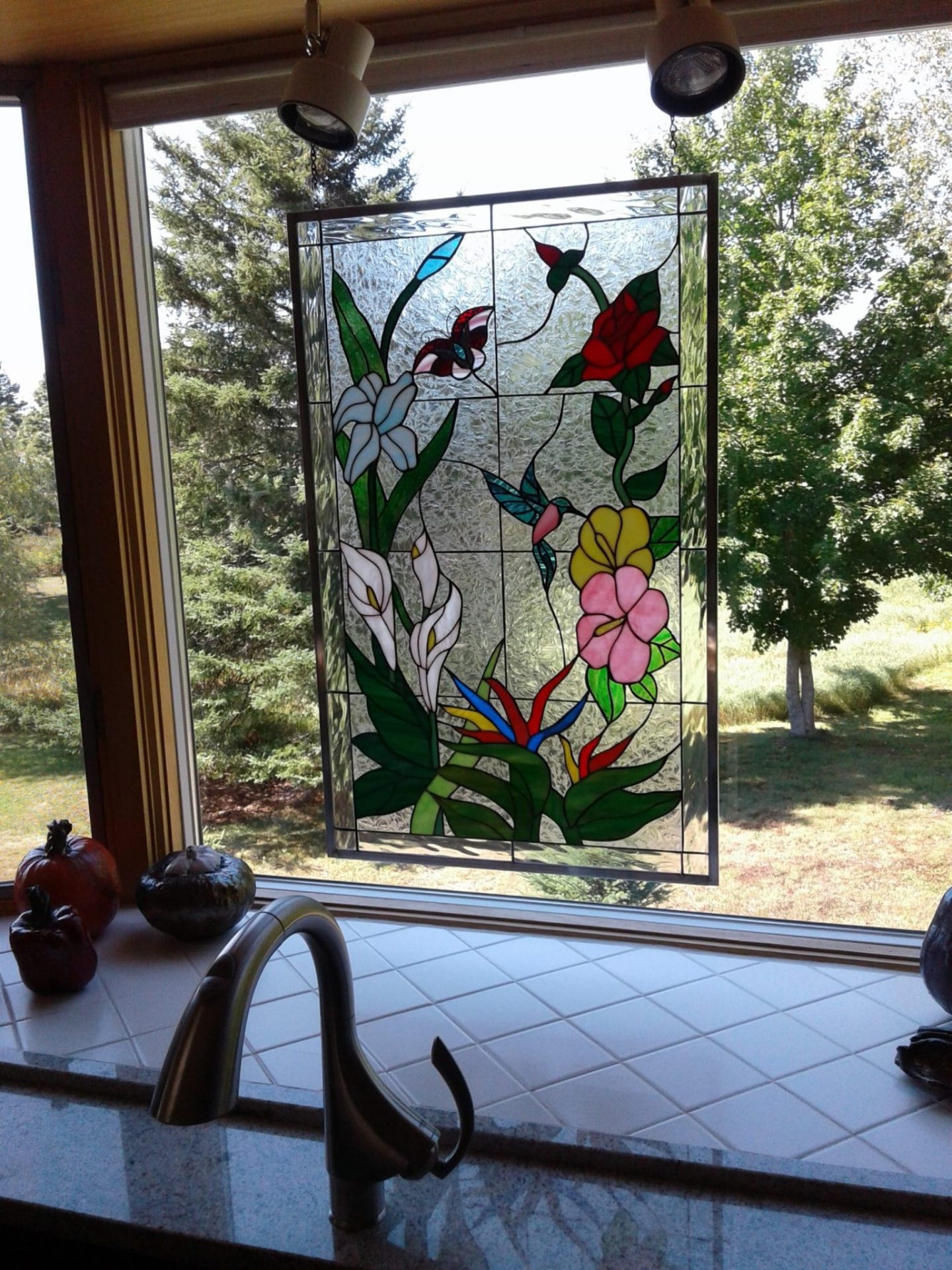 Lovely colorful hummingbirds and flowers stained glass panel hung in a kitchen window with chain