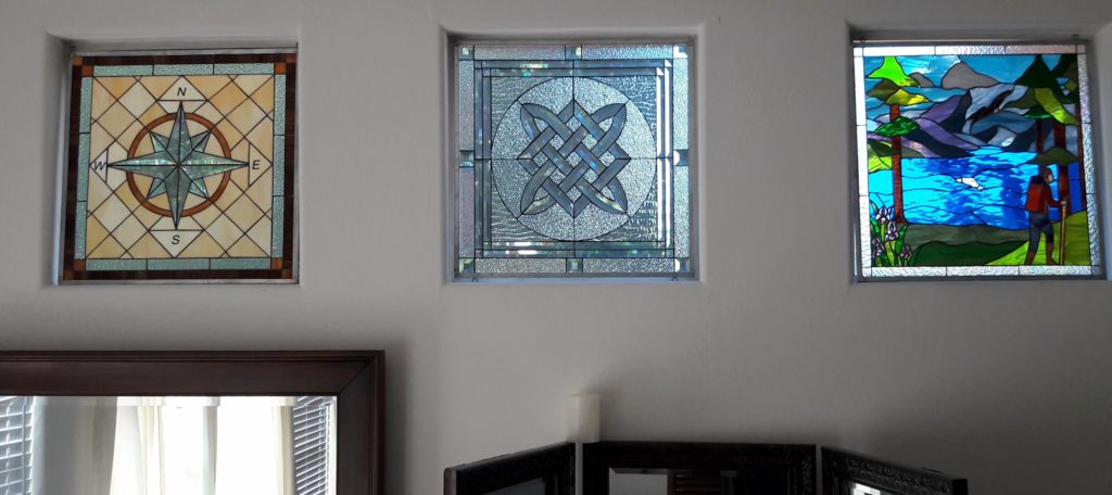 Three stained glass windows simply hung with hooks in front of existing windows