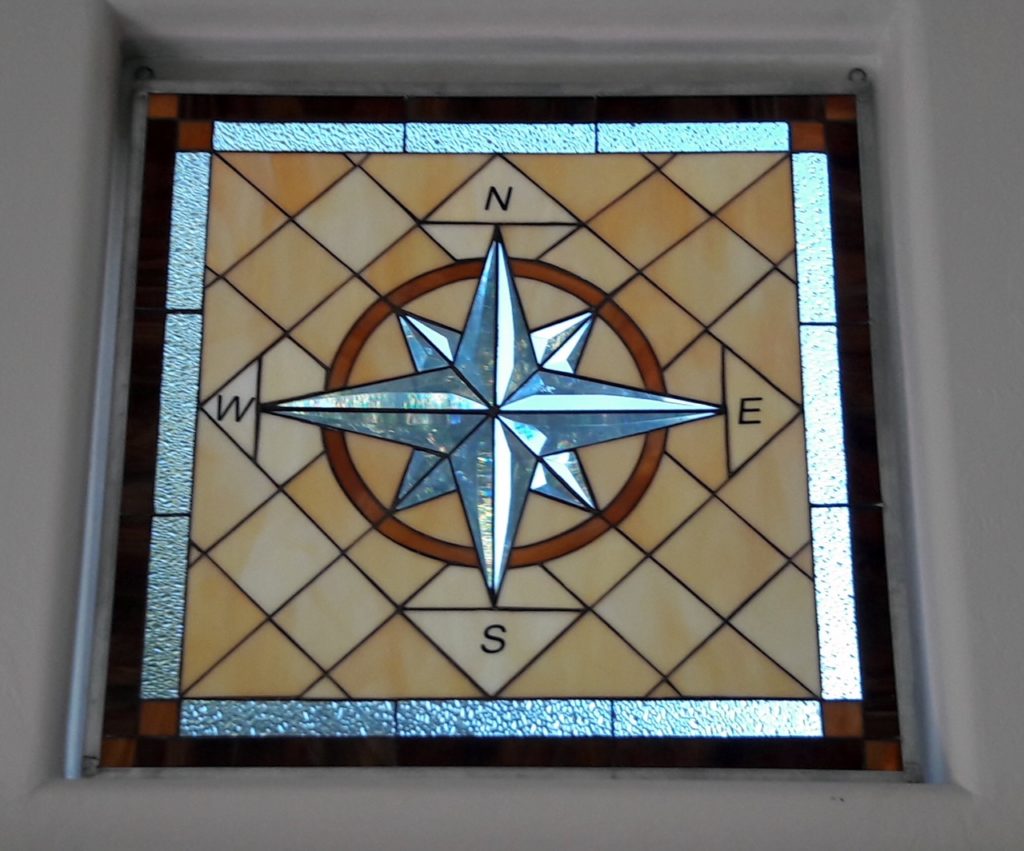 Three stained glass windows simply hung with hooks in front of existing windows