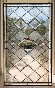 A rectangular stained glass panel featuring clear textured and beveled diamond shapes in a repeating geometric pattern, framed in dark lead.