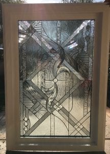 A rectangular clear stained glass panel, showcasing an intricate abstract and geometric design composed of various clear textured, beveled, and heavily textured glass sections. The central motif features elegant swirling clear glass, surrounded by a dynamic mosaic of horizontal, vertical, and diagonal patterns. Many sections include sparkling, faceted glass elements that brilliantly refract light. The panel is set in a light-colored frame, with natural light from outdoors illuminating the textures and creating bright reflections.