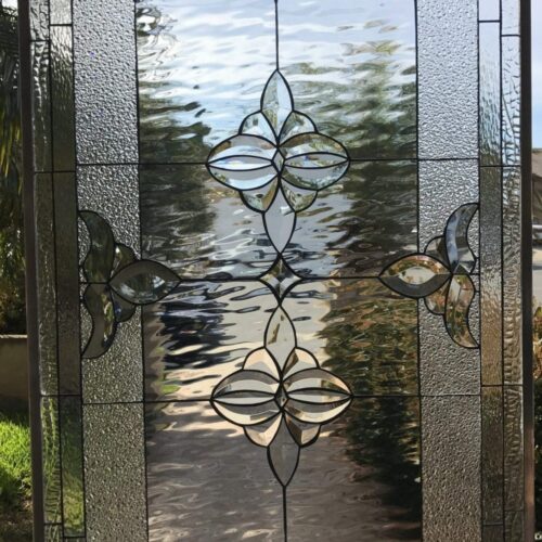A rectangular clear stained glass panel with a symmetrical design. It features a central vertical arrangement of two large, intricate beveled glass floral medallions. Two smaller, partial floral motifs extend horizontally from the sides. The main background sections are clear waterglass, framed by textured clear hammered glass borders and thin clear beveled pieces. All glass pieces are joined by dark lead came.