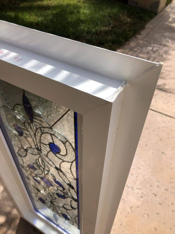 A rectangular stained glass panel featuring an abstract design with swirling clear textured and beveled glass patterns, accented with deep blue oval and teardrop shapes, all enclosed within a sturdy white frame.