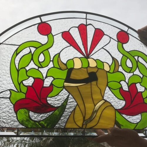 An arched leaded stained glass panel featuring a vibrant Art Nouveau floral design. Swirling green vines interlace with stylized red flowers and two red spherical accents, flanking a central abstract yellow-gold motif. The background is composed of clear, textured glass with scattered clear beveled diamonds, all framed by dark lead lines.