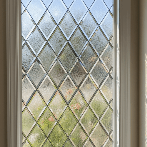 A rectangular stained glass window with a classic diamond lattice pattern. The diamonds alternate in a checkerboard pattern between clear beveled glass and frosty, textured 'glue chip' privacy glass.