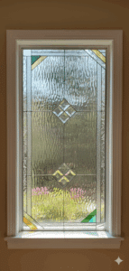 A rectangular clear stained glass window panel with a geometric design, featuring textured glass, beveled diamond shapes, and subtle yellow and green accents, installed in a white window frame.