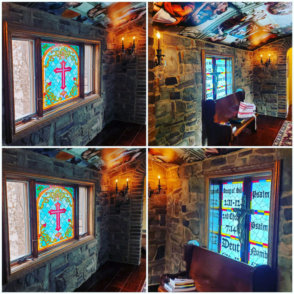 A rectangular window in a stone wall contains an arched stained glass panel. The panel features a central red cross, framed by green and yellow vines, against a light blue background with a diamond pattern. Biblical verses like 'Song of Solomon 2:11-12' and 'Psalm 91' are visibly integrated into the glass, and a dark wooden pew sits below the window.