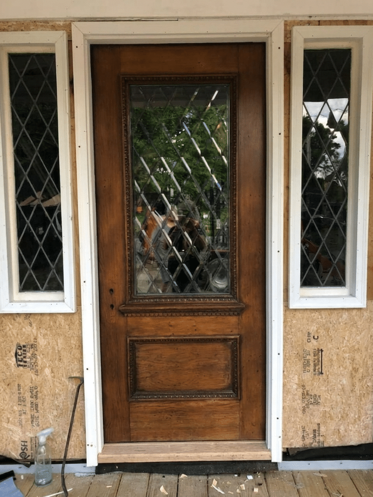 A dark wooden front door with a large rectangular leaded glass insert and two matching narrow rectangular sidelights, all featuring clear beveled diamond-shaped panes.