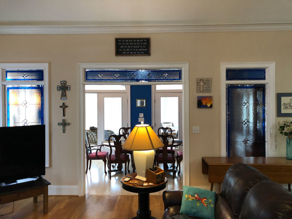 Five custom leaded stained glass panels installed in an interior entryway. The set includes two vertical sidelights flanking the doorway and three horizontal transom panels positioned above the doorway and sidelights. Each panel features a repeating geometric pattern of clear textured and beveled diamond shapes, set against a background of deep blue textured glass, bordered by solid blue glass. The panels enhance privacy while allowing light to filter through.