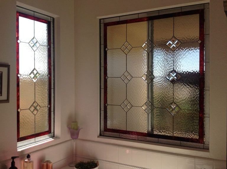 Two rectangular leaded stained glass window panels featuring a geometric design with clear, heavily textured privacy glass, accented by a deep red streaky glass border and small clear beveled diamonds. Slight hints of light blue/green glass are visible within some diamond patterns.