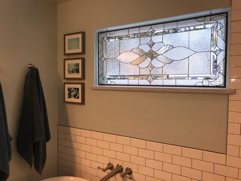 A rectangular clear and textured leaded stained glass transom window, featuring an organic ripple pattern with beveled accents, installed above white subway tiles in a modern bathroom. The window provides privacy while allowing diffused natural light.