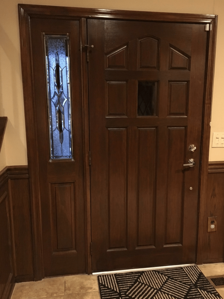 A narrow, rectangular leaded stained glass sidelight panel with clear textured and beveled glass in a geometric design, next to a dark wood door.