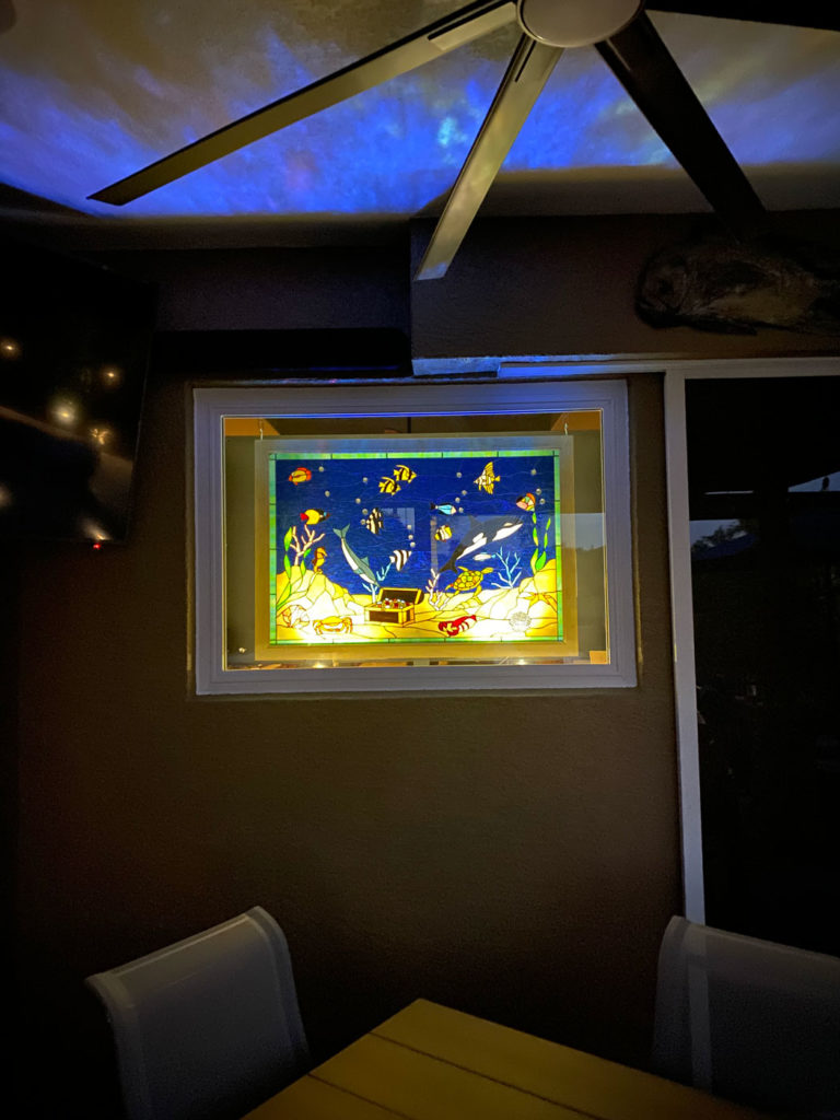 Rectangular stained glass window panel depicting a vibrant underwater scene with a blue dolphin, colorful tropical fish, an open gold treasure chest, red crabs, a green turtle, and coral against a deep blue background.