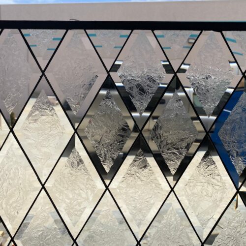 A close-up of a rectangular clear leaded stained glass panel with a repeating geometric pattern of diamond shapes. The diamonds feature highly textured, almost frosted, clear glass, resembling a detailed fern or glue chip pattern. Dark lead lines frame each diamond, creating a classic and elegant design that offers privacy while maximizing light.
