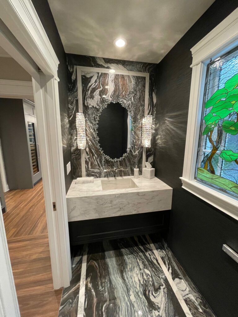 A rectangular stained glass window featuring a naturalistic tree design with vibrant green leaves and textured brown branches, set against a light blue, rippled glass background, installed in a white-framed window.