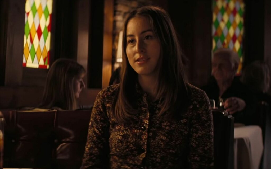 A narrow, rectangular leaded stained glass panel featuring a repeating diamond (harlequin) pattern in alternating red, green, and clear/yellow textured glass, set within a dark wooden frame in a dimly lit interior.