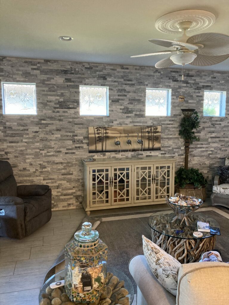 Four rectangular clear textured and beveled stained glass panels depicting a tropical palm tree and a circular sun/moon motif, set into a gray stacked stone accent wall above a white console table in a living room.