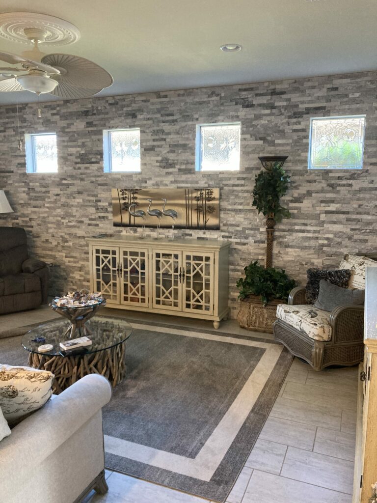 Four rectangular clear textured and beveled stained glass windows featuring subtle leaf and circle patterns, installed high on a grey stone accent wall in a coastal-themed living room.