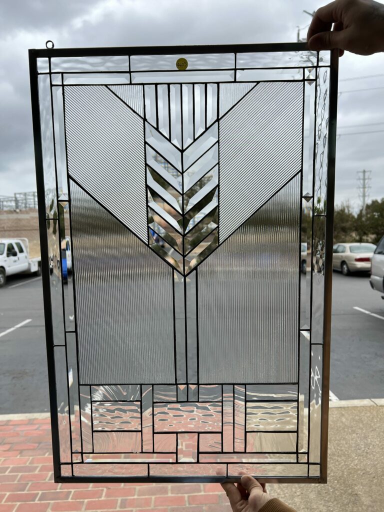 A rectangular leaded stained glass panel with a clear, geometric design, featuring a central chevron pattern of beveled glass, flanked by vertical and diagonal reeded glass, and borders with clear beveled and wavy textured glass.