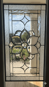 A rectangular, leaded clear stained glass panel featuring a central floral medallion crafted from beveled glass, surrounded by textured clear glass and smaller diamond-shaped bevels.