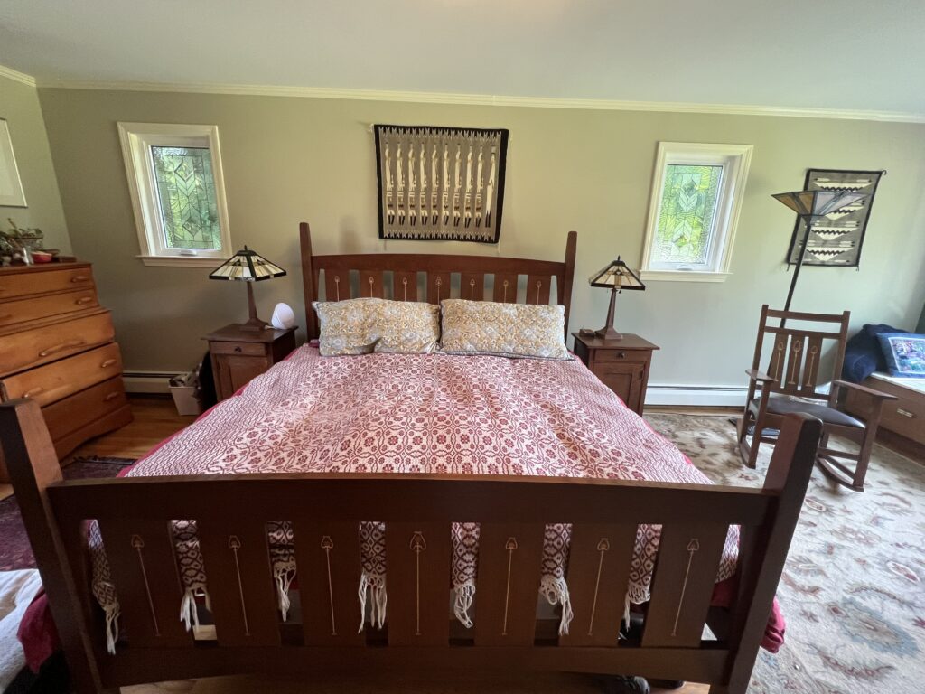Two rectangular clear stained glass window panels installed in a bedroom. Each panel features a repeating geometric pattern of textured and possibly beveled glass, creating abstract leaf or chevron shapes. The overall style is reminiscent of Arts and Crafts.