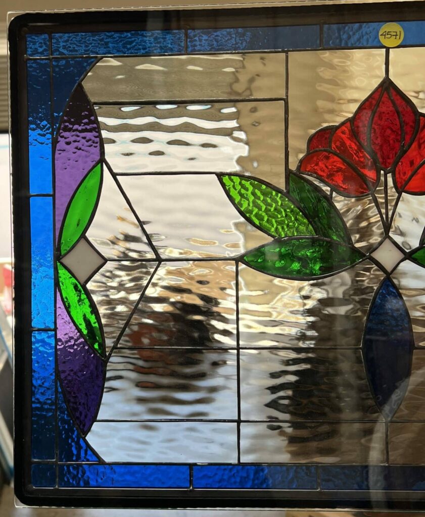 A rectangular leaded stained glass panel featuring vibrant red poppy-like flowers and green leaves, set against a clear textured background with deep blue and purple accents.