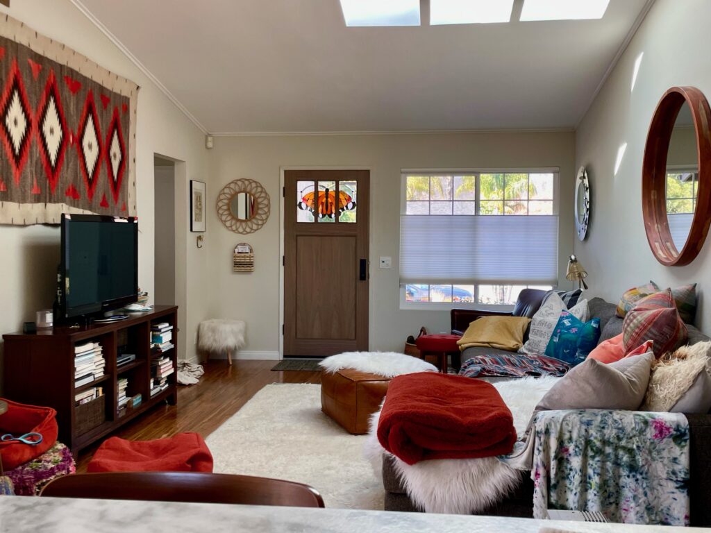 A rectangular stained glass transom panel featuring a detailed Monarch butterfly design with vibrant orange, black, and white glass pieces, set into a dark wood front door in a cozy living room.