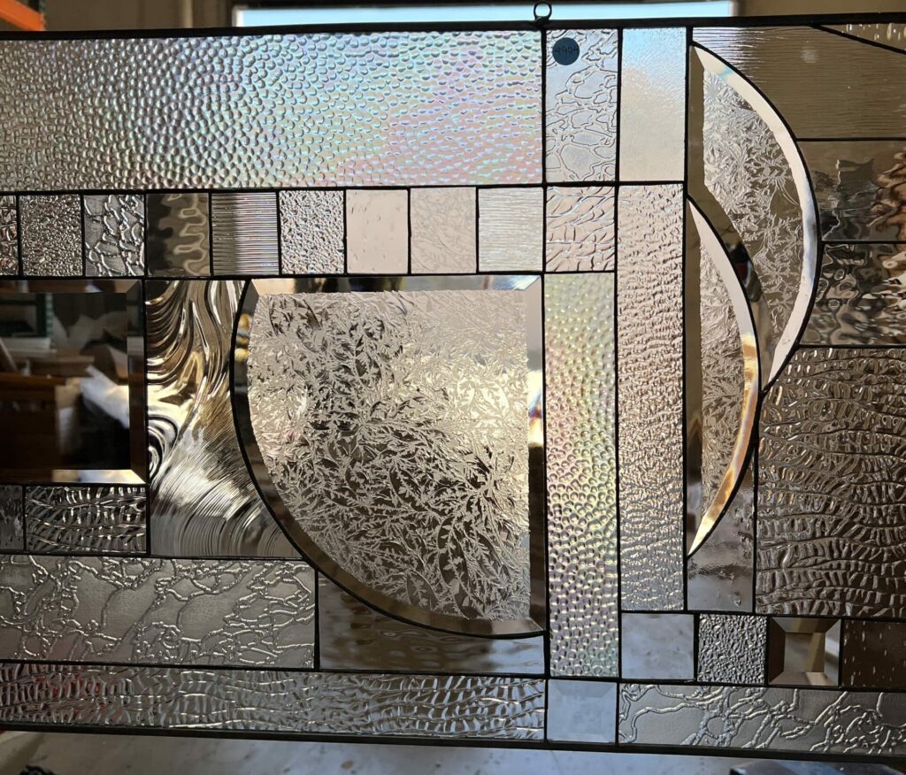 A rectangular clear leaded stained glass panel with a modern abstract design. It features large intersecting curved and circular elements along with rectangular sections, all composed of various clear textured glasses like pebbled, wavy, rippled, and frosted fern patterns, creating light distortion.
