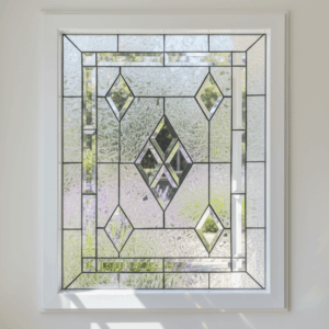 A rectangular leaded stained glass window set in a white frame, featuring a central cluster of clear diamond bevels, surrounded by textured clear glass and four additional clear diamond bevels.