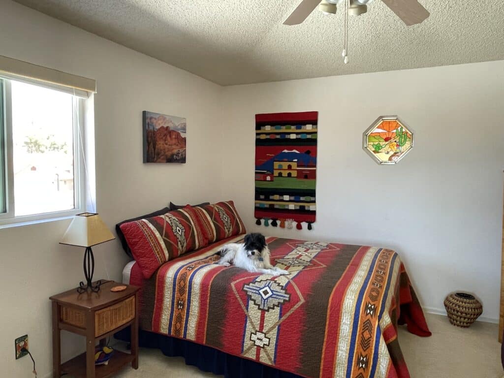 An octagonal stained glass panel with a metallic frame, depicting a vibrant desert landscape. The design features green saguaro cacti in the foreground, with rolling orange and red mountains under a bright yellow sun descending into a gradient orange and yellow sky.
